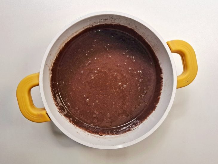 Leite condensado, amido e chocolate em pó misturados em uma panela.