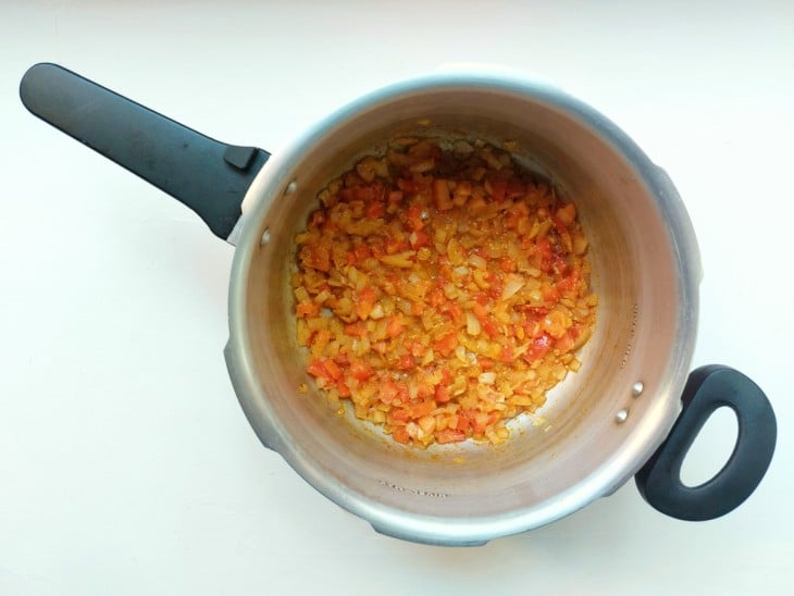 Tomate, cebola, azeite e outros temperos na panela de pressão.