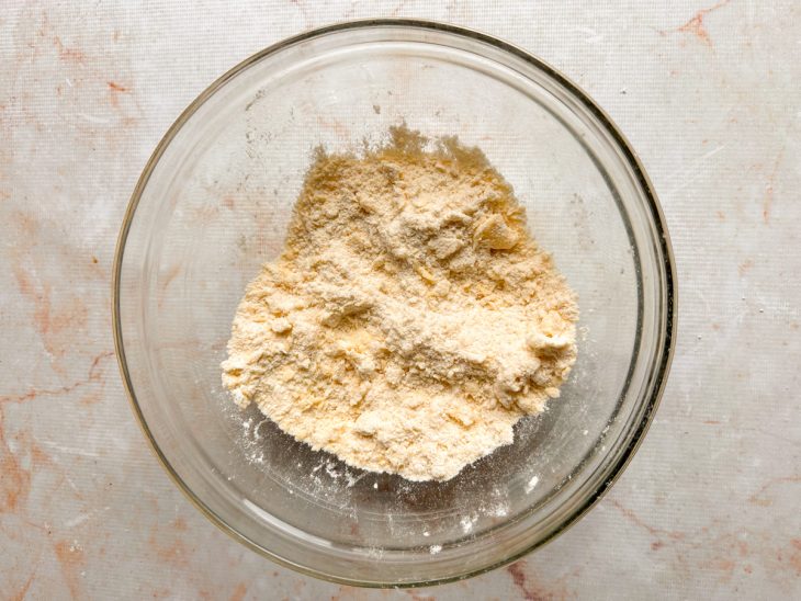 Farinha, manteiga e sal sendo misturados até formar uma farofa úmida.