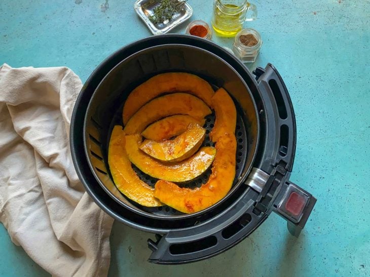 Uma cesta de airfryer contendo fatias de abóbora temperadas.