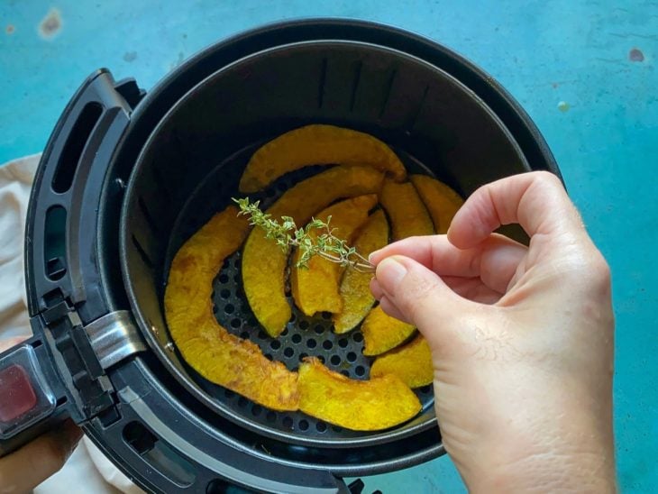 Uma cesta de airfryer contendo fatias de abóbora temperadas.