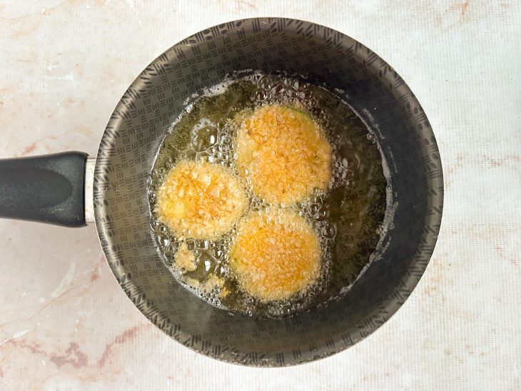 Fatias de abobrinha sendo fritas no óleo da panela.