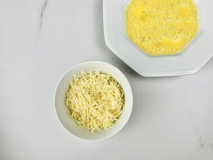 Ovo batido em um recipiente e queijo parmesão ralado em outro.
