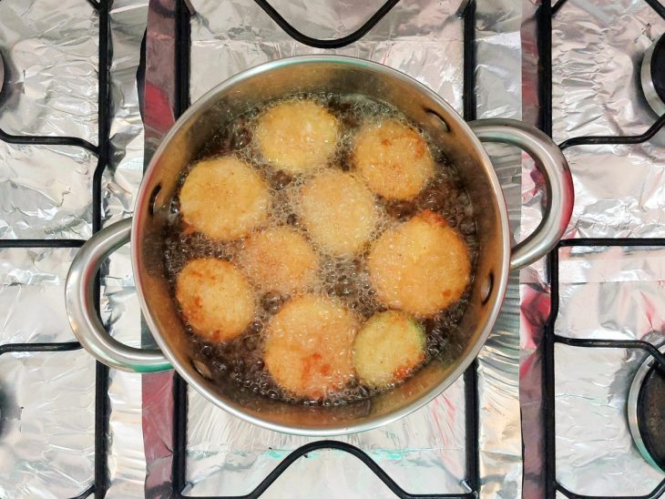 Uma panela com óleo e fatias de abobrinha fritando.