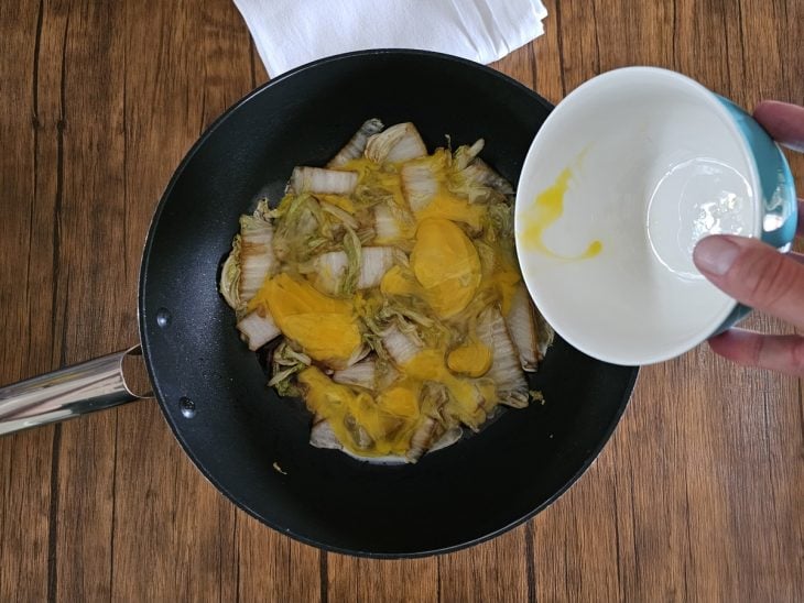 Uma frigideira com acelga, ovos e temperos refogando.