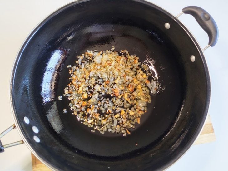 Uma frigideira com azeite, cebola e alho a dourar.