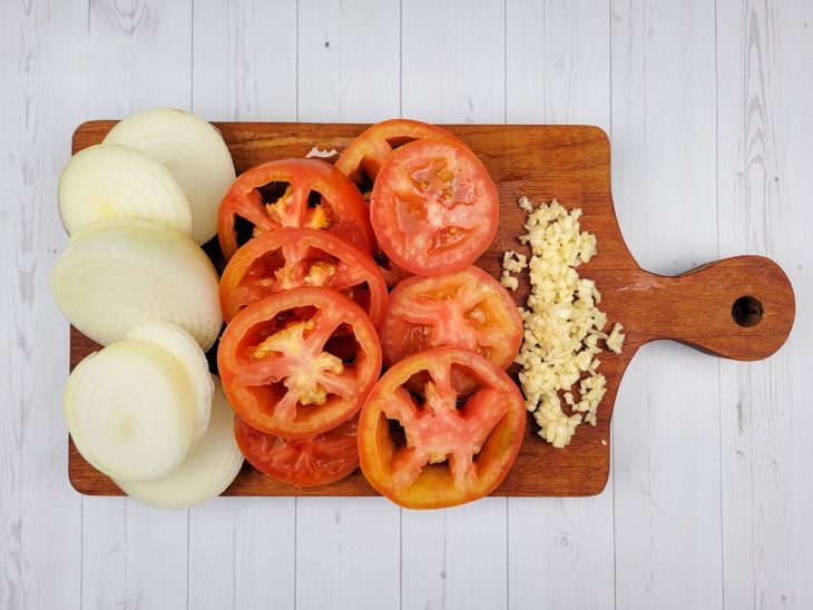 Uma tábua com alho, tomate e cebola fatiados.