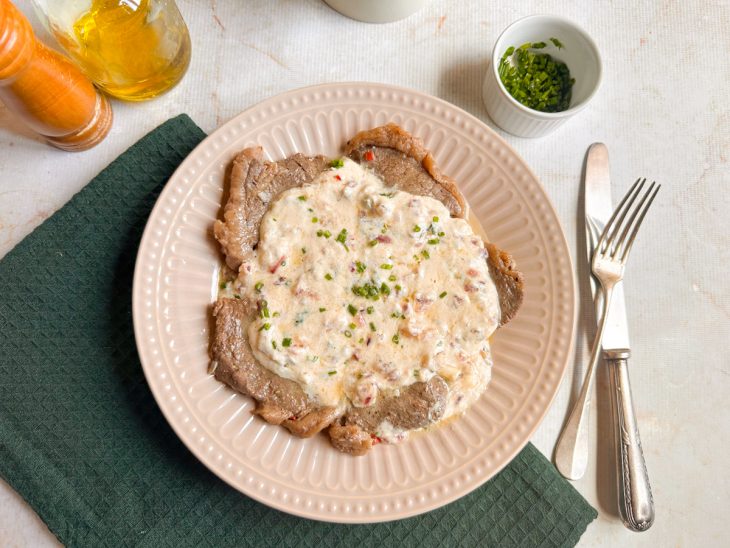 Alcatra pronta, servida com molho de queijo por cima.