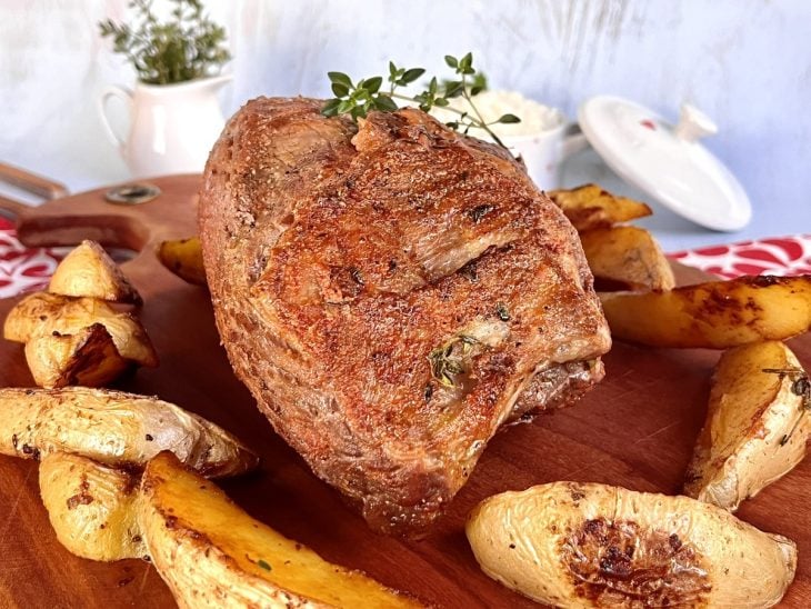 Uma tábua contendo alcatra no forno com batatas.