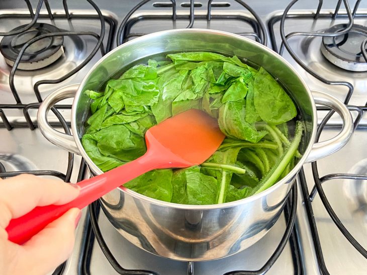 Uma panela com água e folhas de almeirão cozinhando.