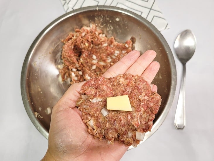 Uma porção da massa de carne aberta com um cubinho de queijo no meio.