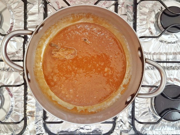 Açúcar derretido, canela e cravos em uma panela.