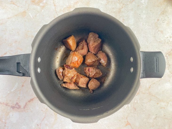 Cubos de carne selados no azeite em uma panela de pressão.