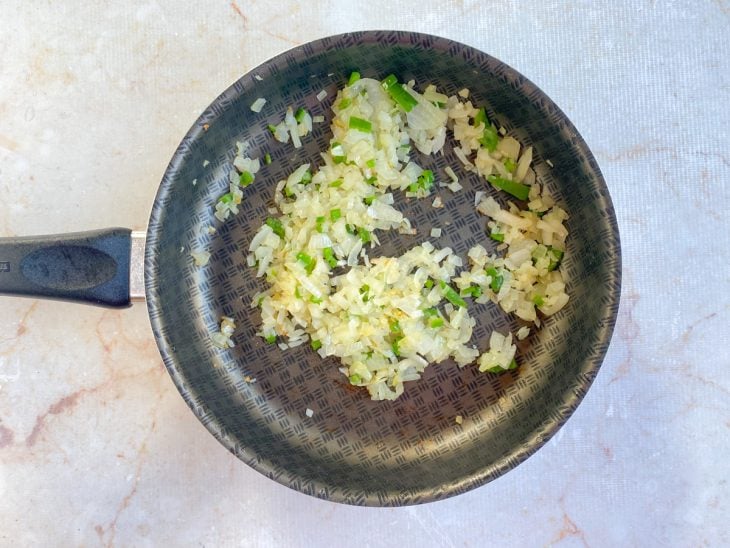 Cebola e pimentão refogados com azeite em uma frigideira.
