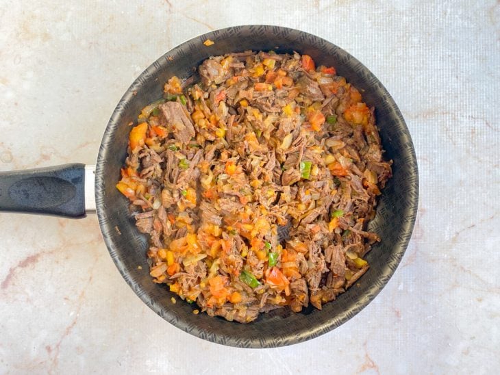 Carne desfiada, tomate e temperos adicionados na panela com refogado de cebola e pimentão.