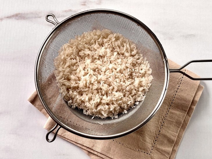 Grãos de arroz lavados e escorridos na peneira.