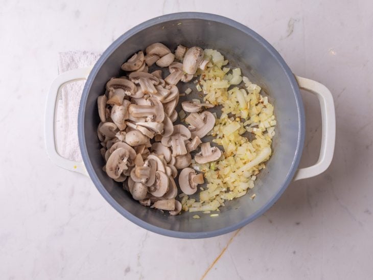 Uma panela com azeite, cebola e cogumelos refogando.