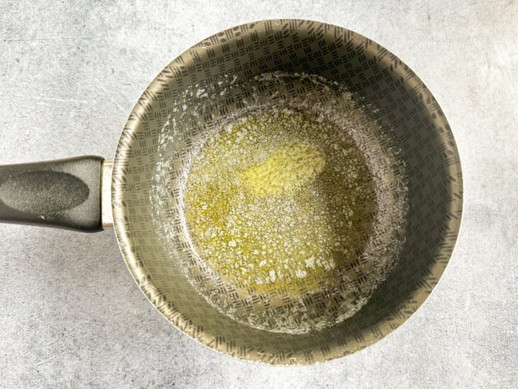 Manteiga derretendo em fogo médio dentro de uma panela de alumínio.
