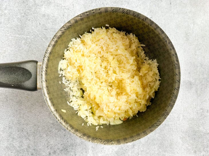 Arroz parboilizado sendo despejado na panela e misturado ao refogado inicial.