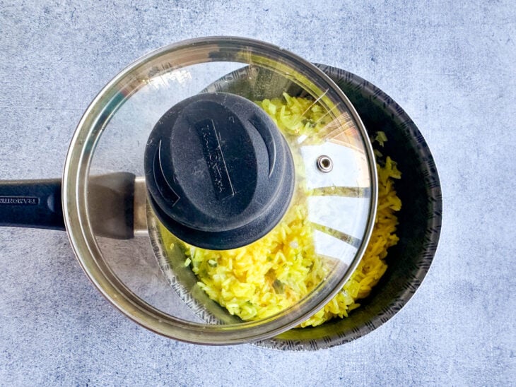 Panela semiaberta mostrando o arroz cozinhando no líquido amarelo em ebulição.