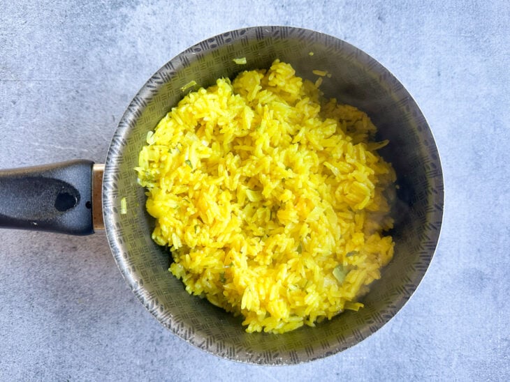 Garfo soltando os grãos do arroz amarelo bem cozido dentro da panela.