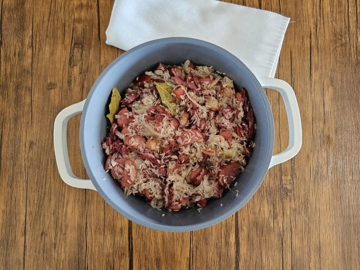 Panela com arroz, carnes e temperos misturados.