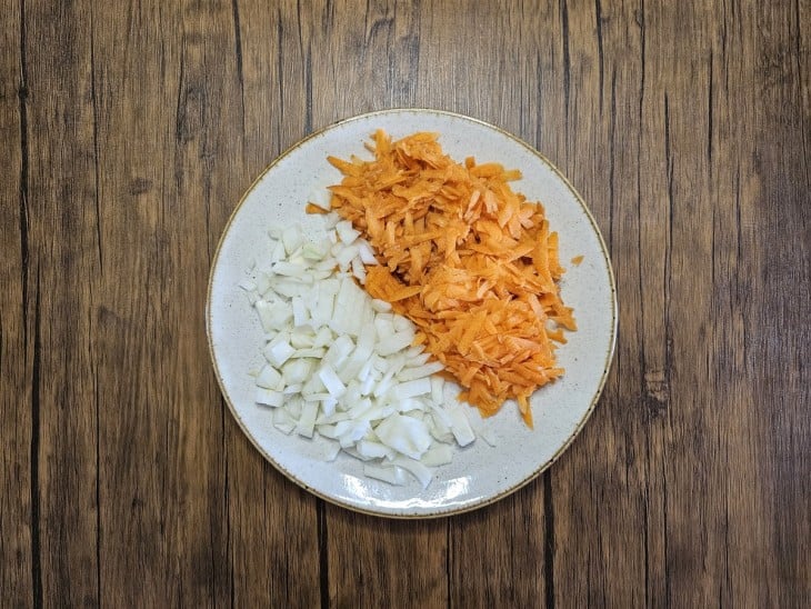 Cebolas picadas e cenouras raladas em um mesmo prato.