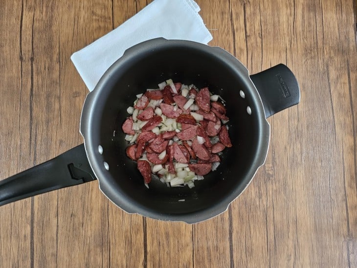 Uma panela de pressão com calabresa e cebola.