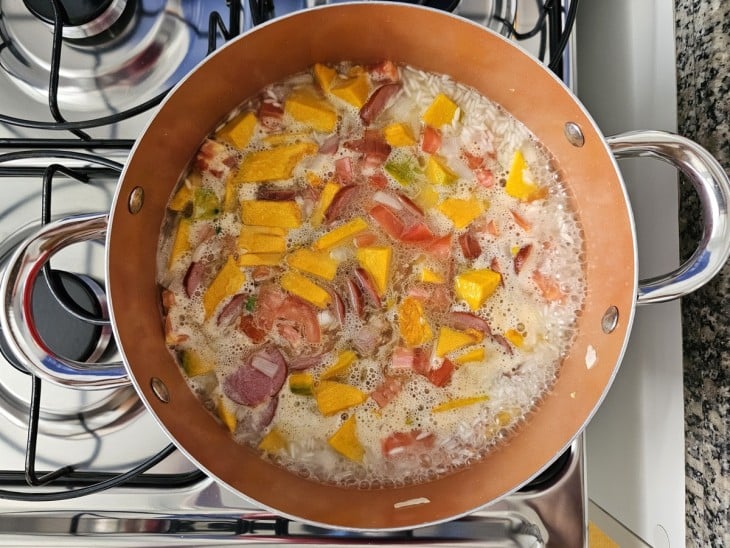 Uma panela contendo abóbora, calabresa, bacon, arroz, sal, tomate e água.