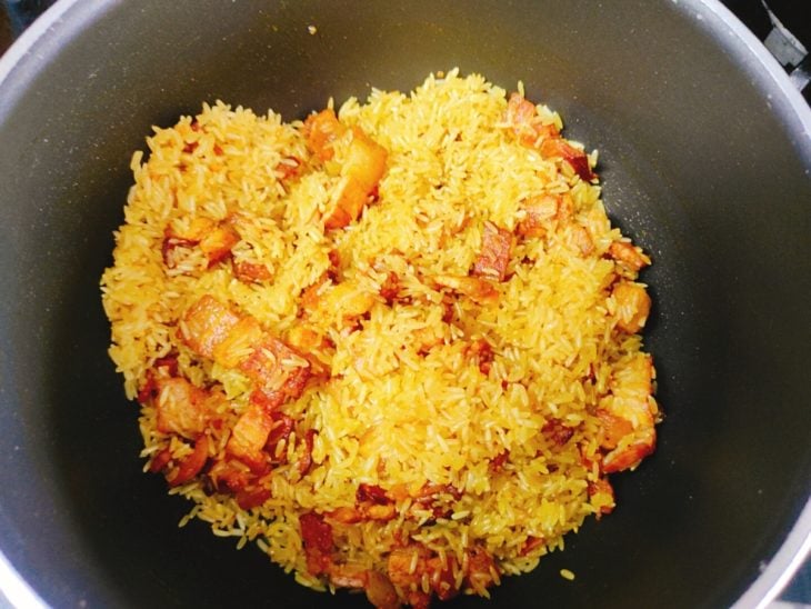 Uma panela com bacon, arroz e temperos.