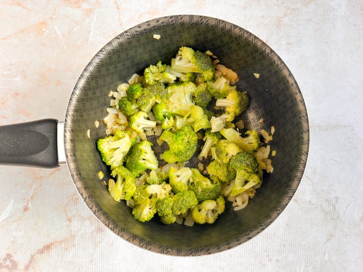 Brócolis colocado na panela com alho e cebola refogados.