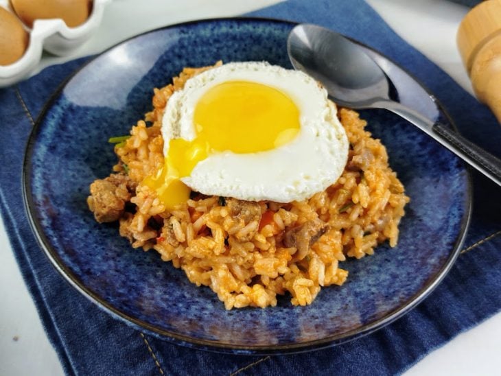 Arroz com moela servido com um ovo frito sobreposto num prato redondo azul.