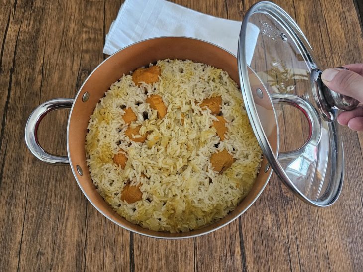 Panela com arroz e pequi sendo fechada.