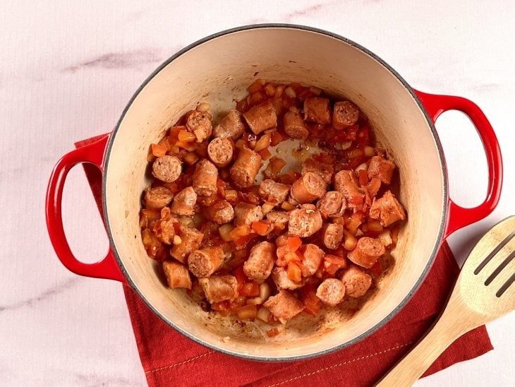 Uma panela contendo linguiças picadas, alho, cebola e tomate.