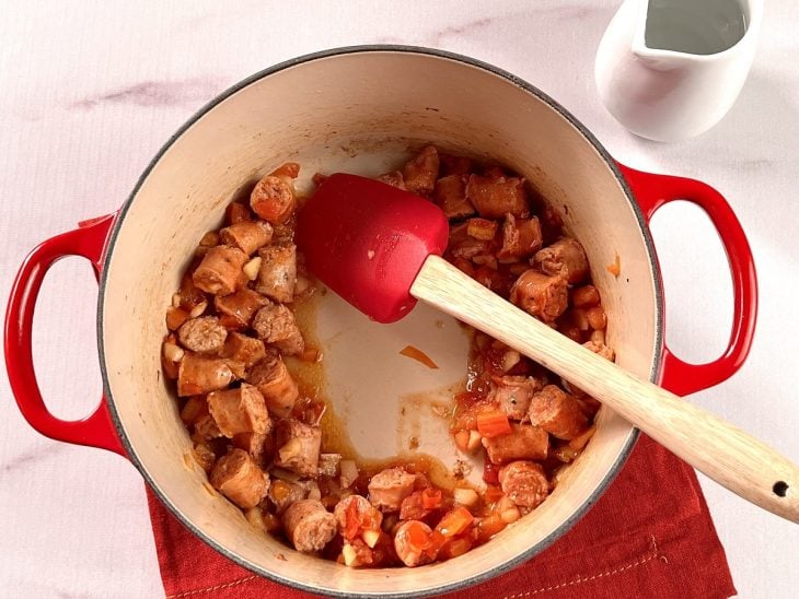 Uma panela contendo linguiças picadas, alho, cebola e tomate.