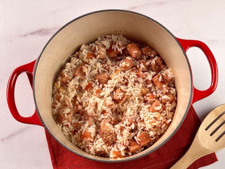 Uma panela contendo linguiças picadas, alho, cebola, tomate e arroz.