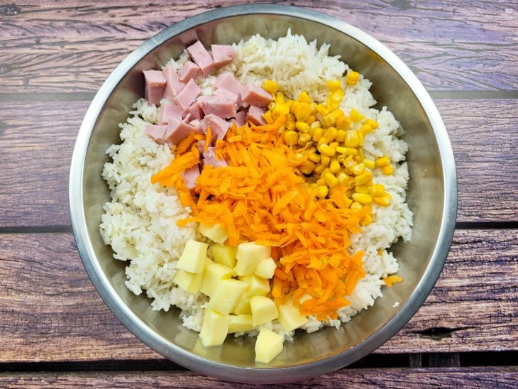 Um recipiente contendo arroz cozido, presunto, mussarela, milho e cenoura.
