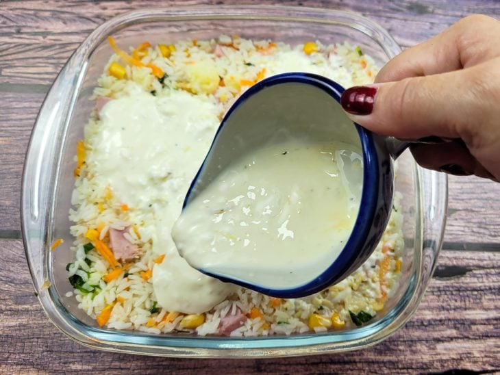 Um refratário contendo a mistura com arroz sendo coberta com o creme.