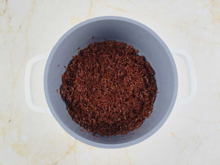 Arroz vermelho sendo refogado com óleo em uma panela em fogo médio.