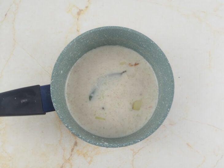 Leite aquecendo em fogo baixo em uma panela menor com cebola, louro e especiarias.