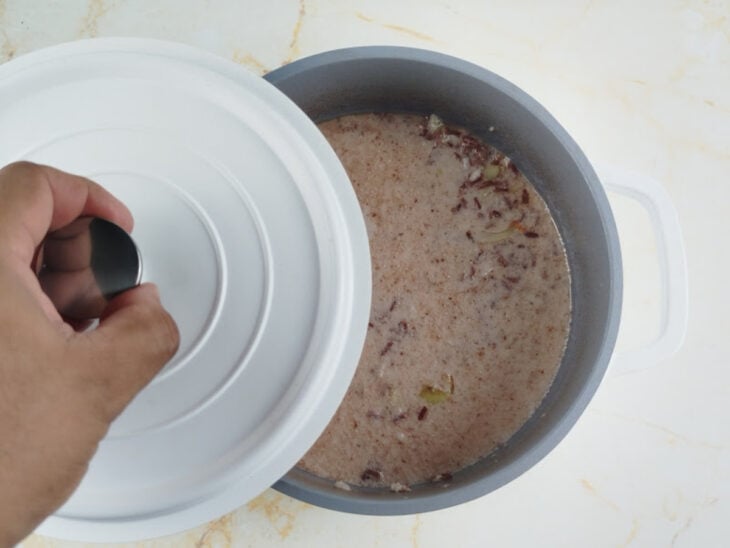 Arroz cozinhando parcialmente tampado no leite até reduzir o líquido.