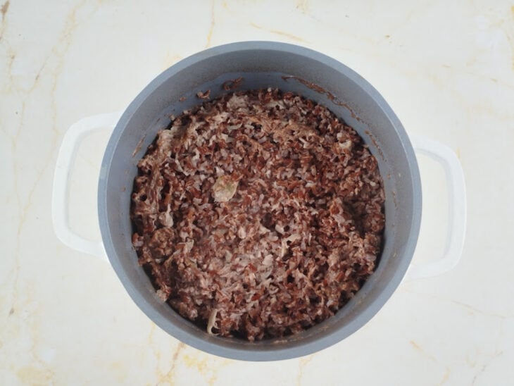 Garfo soltando os grãos de arroz vermelho cozidos e úmidos na panela.