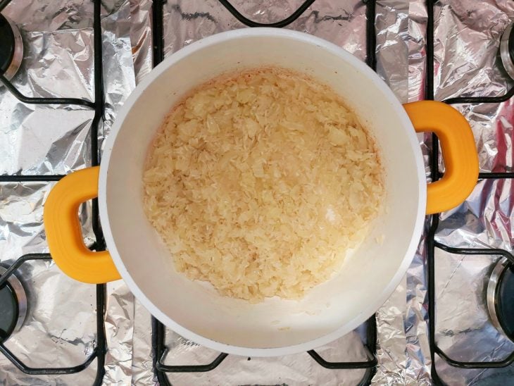 Uma panela refogando arroz, cebola e alho.
