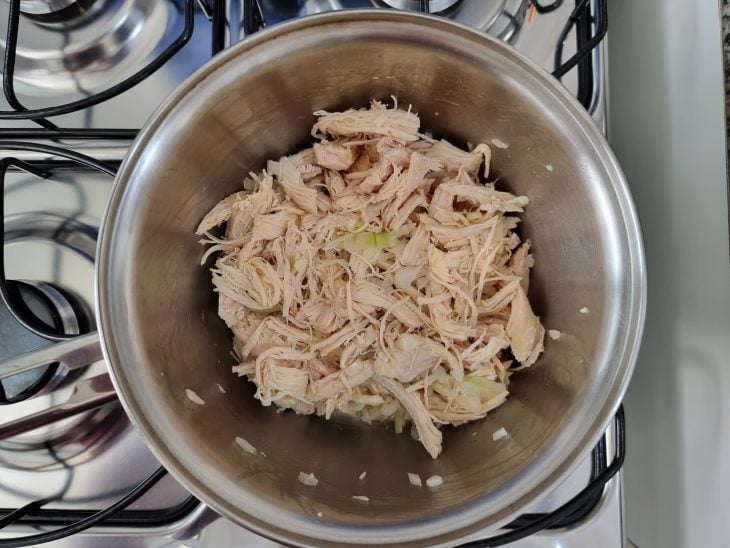 Panela com frango desfiado e temperos.