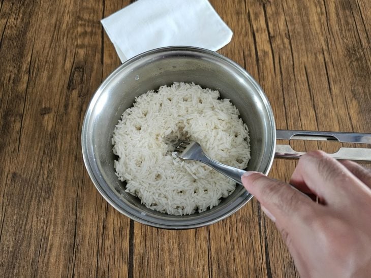 Panela de com arroz pronto - mão utilizando garfo para verificar se toda água secou.