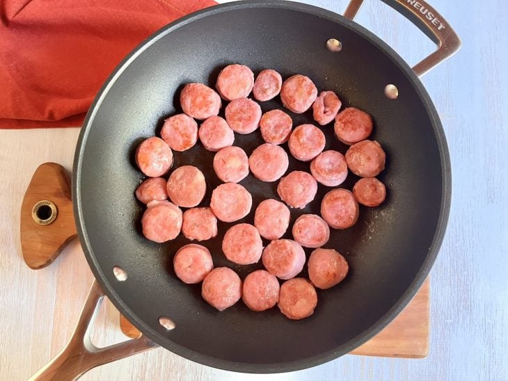 Uma panela fritando rodelas de linguiça.