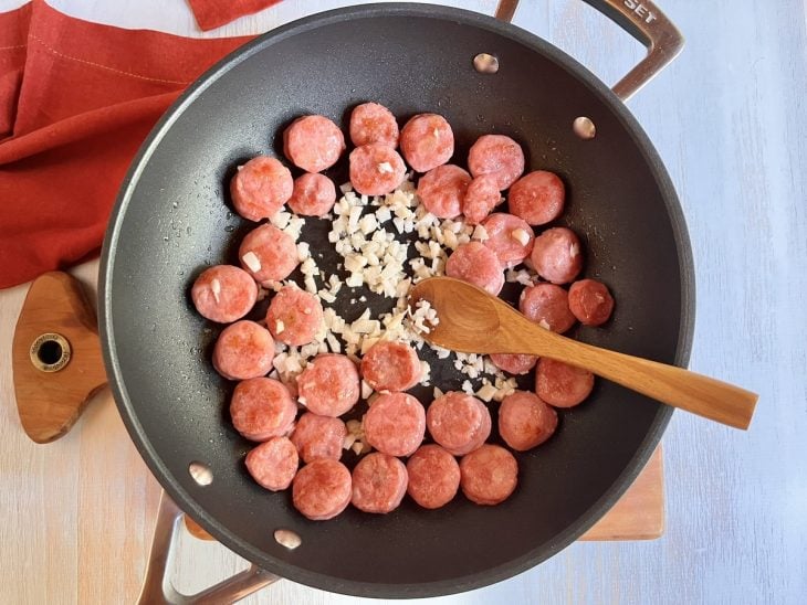 Uma panela refogando rodelas de linguiça e cebola.