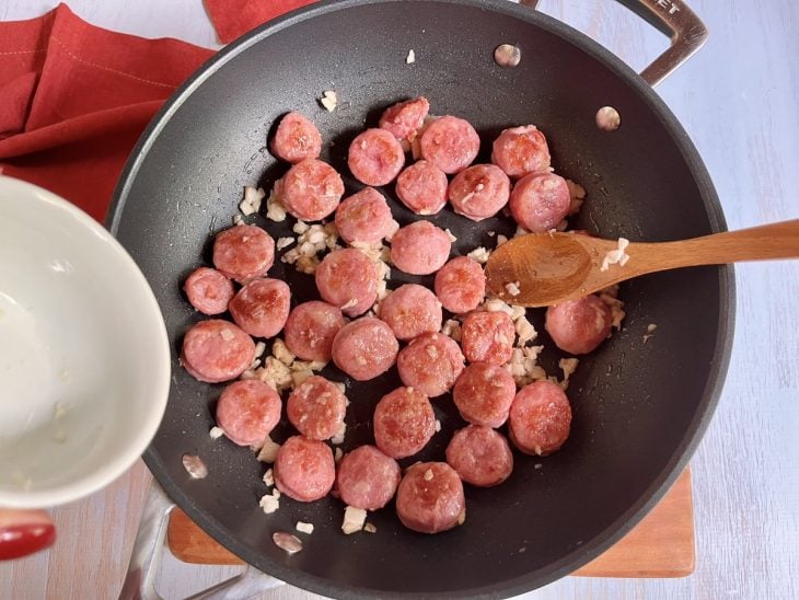 Uma panela refogando rodelas de linguiça e cebola.