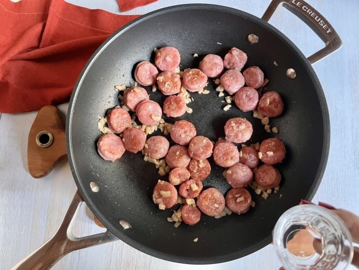 Uma panela flambando rodelas de linguiça e cebola.