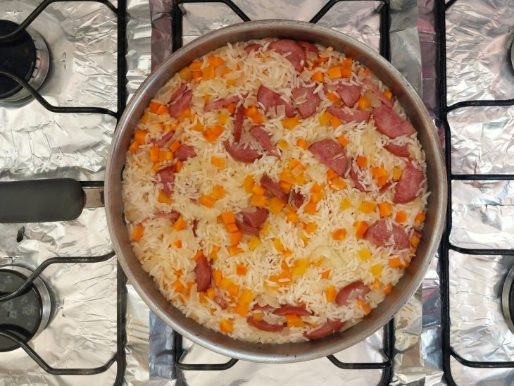 Uma panela refogando calabresa, cebolas, legumes e arroz.